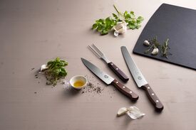 Auf einer Arbeitsplatte liegen eine Fleischgabel, ein Fleischmesser und ein Brotmesser.