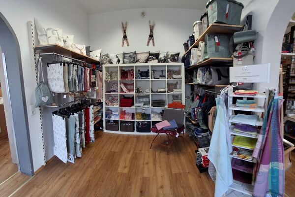 Ein Laden mit Regalen voller Kissen, Stoffrollen und Taschen auf Holzfußboden.